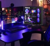 Bureau gaming avec PC transparent aux composants RGB, double ecran, clavier mecanique et fauteuil gamer dans une ambiance bleu violet